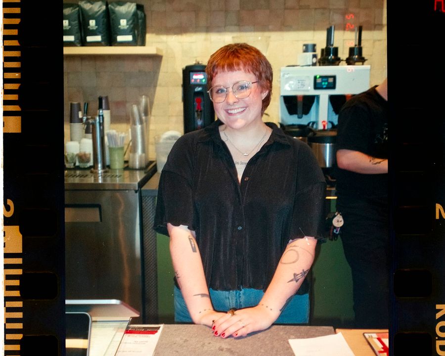 A smiling coffee shop owner standing behind the counter of her cafe