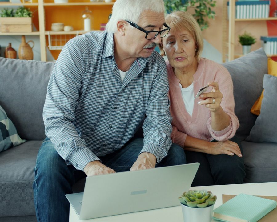 An older couple paying their bills online together on a laptop at home