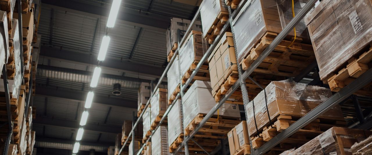 Cardboard boxes of stock stacked on white metal warehouse racking